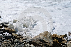 A lot of white foam from the big storm waves on the seashore among the cobblestones.