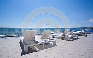 A lot of white sunbeds at the balcony of a luxury hotel. White deck chairs near the tropical beach. Summer vacation.