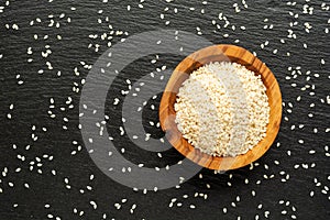 Lot of whole unpeeled sesame seeds in wooden bowl flat lay on slate background
