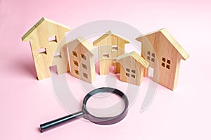 A lot of wooden houses on a pink background and a magnifying glass. The concept of finding a new home to buy or property to invest