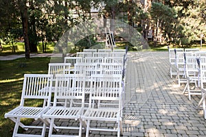 A lot of wooden white chairs near the platform for a wedding ceremony under the open sky. Chairs