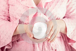 Lotion for hands, cream for face and body moisturizing is held by a woman in a bathrobe in the bathroom