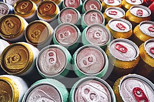 Lots of aluminum cans in the ice in the open fridge. Drops of water on a cold can of drink. Metal cans of beer with ice cubes in photo