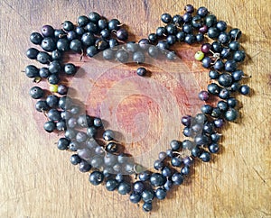 Lots of black currants on a wooden table in the shape of a heart.