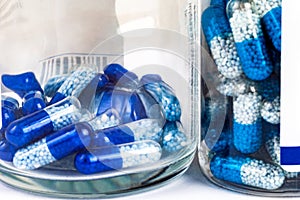 Lots of blue-white pills, transparent tablets with granules in a see through bottle containers seen from the side, macro, closeup