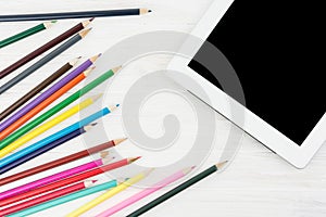 Lots Of Colorful Pencils NExt To Big Screen Tablet On White Wood