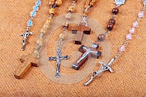 Lots of different styled Christian crosses, multiple rosaries laying on brown background Prayer and belief, christianity symbols