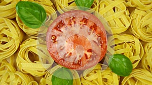 Lots of dry tagliatelle pasta, garnished with basil leaves and cut tomato in center of circle, rotate counterclockwise