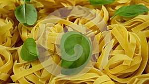 Lots of dry tagliatelle pasta, garnished with basil leaves , rotate of circle counterclockwise.