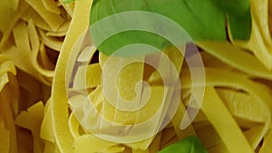 Lots of dry tagliatelle pasta, garnished with basil leaves , rotate of circle counterclockwise. Vertical video.