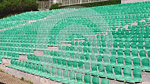 Lots of empty seats in old open-air theater theater. Plastic green seats are arranged in a rows.