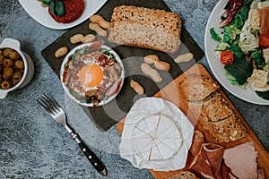 Lots of food and dishes in the background. Meat platter and Camembert cheese with baguette. Salad with prosciutto. Olives. Perfect