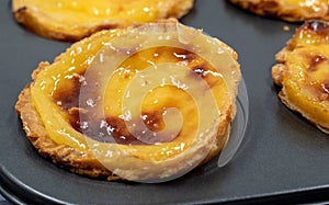 Lots of freshly baked Pastel de nata or Portuguese egg tart desserts in a baking dish. Pastel de Belme is a small pie