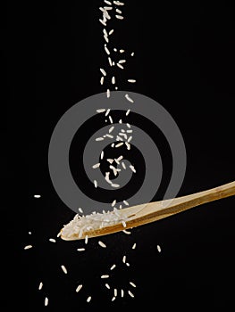 Lots of grains of white rice in a frozen flight on a wooden spoon. Isolated on black background. Grains, cereals, ingredient for