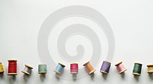 Lots of multicolored threads on old-fashioned wooden reels on a white background with space for text. One of the thread reels is