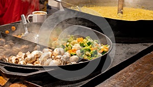 Lots of mushrooms and vegetables frying cooking on a pan, steam over hot food, street food festival market stall outdoors, detail