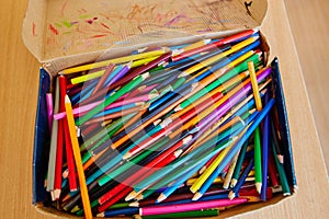 Lots of old colored wooden pencils in a cardboard box with children`s doodles