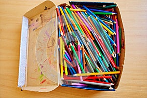 Lots of old colored wooden pencils in a cardboard box with children`s doodles