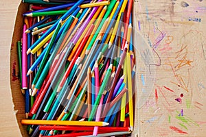 Lots of old colored wooden pencils in a cardboard box with children`s doodles