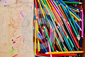 Lots of old colored wooden pencils in a cardboard box with children`s doodles