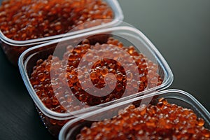 Lots of red caviar in jar. Sea food. Healthy eating. Red salmon caviar. Caviar in bowl over black background. Close-up.