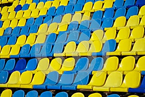 Lots of used blue and yellow plastic seats in an open stadium. Free access. Empty seats, without spectators. Waiting for the sight