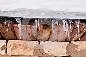 Lots of white long icicles on visor of roof of wooden house in spring