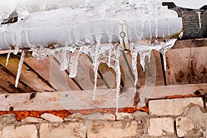 Lots of white long icicles on visor of roof of wooden house in spring