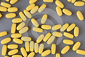 Lots of yellow long vitamins or pills on gray background, close-up, top view. Nutritional supplements concept, health, vitamins,