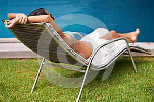 Lounging by the pool. Rear view of a beautiful young woman relaxing in a lounge chair by a swimming pool.