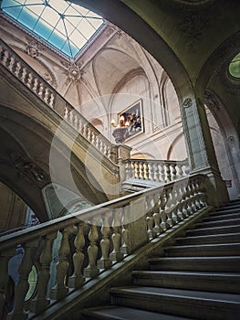 Louvre Palace architectural details of a hall with stone staircase, ornate railings and glowing vintage lamps, Paris, France