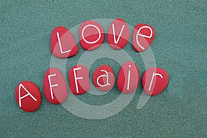 Love affair text composed with carved and red colored stones over green sand