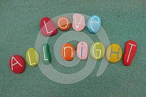 Love all night text composed with multi colored stones over green sand