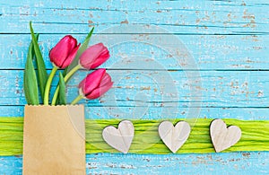 Love background with rustic wooden hearts and red tulips flowers on light blue wood