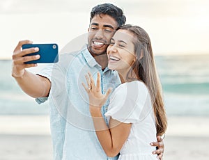 Love, beach and couple after their engagement taking a selfie on a phone while on summer vacation. Happy woman showing