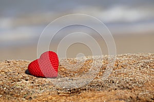 Love on the beach, red knitted heart on blue sea background