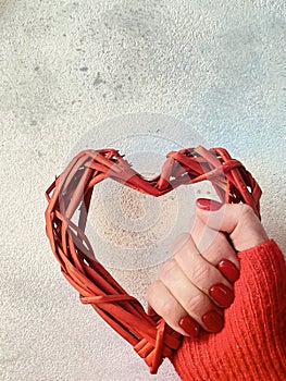 Love care concept. Wooden weaved red heart hold by womenâ€™s hands. Red colored nails.