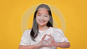 Love and charity. Cute little asian girl showing heart gesture and smiling to camera, expressing kindness