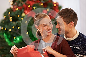 Love, Christmas gift and couple in living room at home for festive celebration together. Smile, happy and young man and