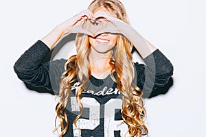 Love. Closeup portrait smiling happy young woman with long blon hair, making heart sign, symbol with hands white wall background.