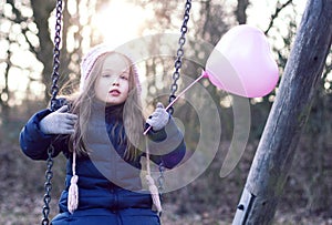 Love concept: child on a swing holding a heart-shaped baloon.
