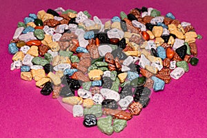Love concept.Heart-shaped decoration from colorful pebbles on a pink background.choco rocks looks like pebbles
