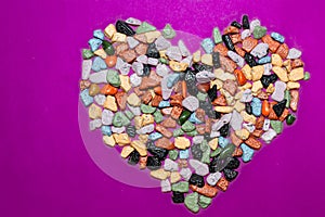 Love concept.Heart-shaped decoration from colorful pebbles on a purple background.choco rocks looks like pebbles