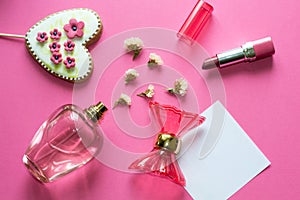 Love concept - pink adorable perfume, gingerbread heart, lipstick, flowers on pink background. Copy space for text. Woman make up