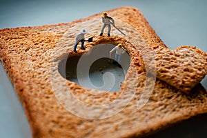 Love Concept. Sad Relationship. Group of Worker Miniature Fixing a Burned Sliced Toasted Bread with a Heart shape