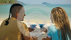 The love couple is holding a glass of blue curacao cocktail, on