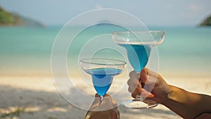 The love couple is holding a glass of blue curacao cocktail, on sea. Man and woman drink alcohol on sand beach. Summer