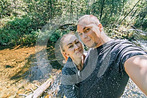 Love couple make selfie on phone. Woman and man traveler in summer passes on wooden log bridge in background of forest