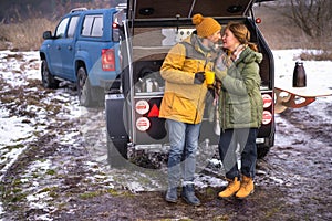 In love couple romantic journey winter camper vacation, man kisses woman while drinking hot tea in cups standing at mini