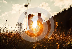 In love couple silhouets among high grass on sunset meadow